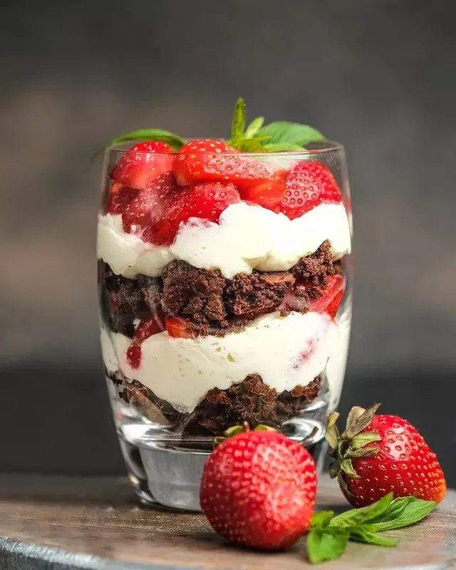 Copo com camadas de brownie, creme branco e morangos frescos por cima