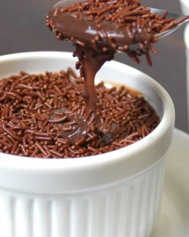 Colher puxando brigadeiro cremoso de um potinho branco coberto de granulado